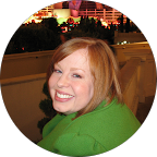 Smiling woman with red hair wearing a green jacket at an outdoor evening event.