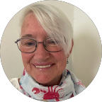 Smiling woman with short white hair, glasses, and a colorful scarf.