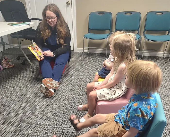 Older woman wearing an audiometric testing headset sitting in a chair with a technician standing beside her.
