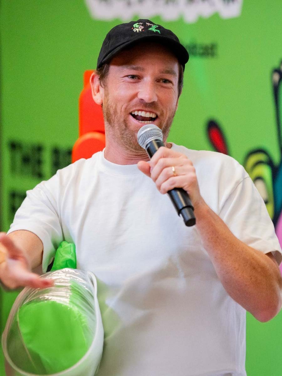 Young man with red hair and beard standing outdoors with arms crossed, wearing a black graphic T-shirt and a watch.