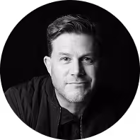 Black and white portrait of a man with short hair and a slight smile against a black background.