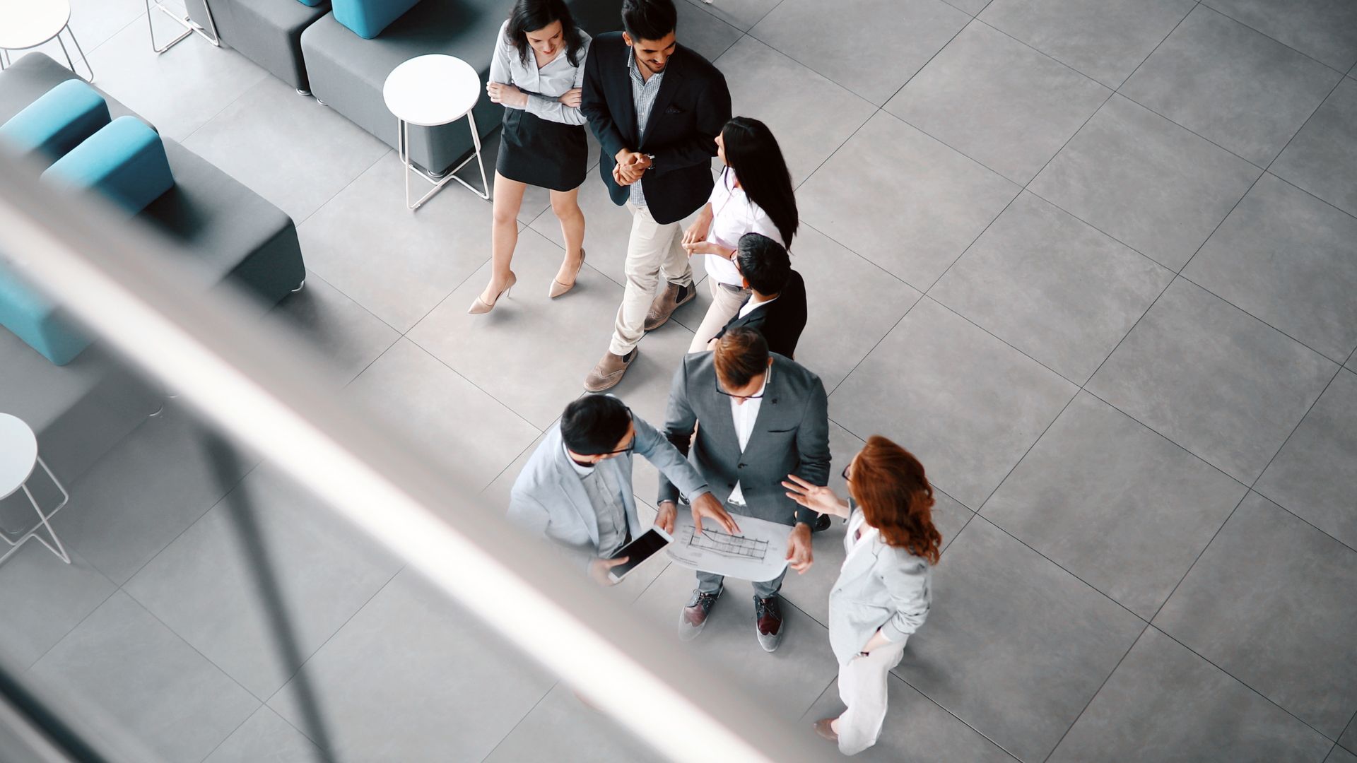 Sechs Geschäftspersonen stehen in einem modernen Büro und betrachten gemeinsam einen Bauplan.