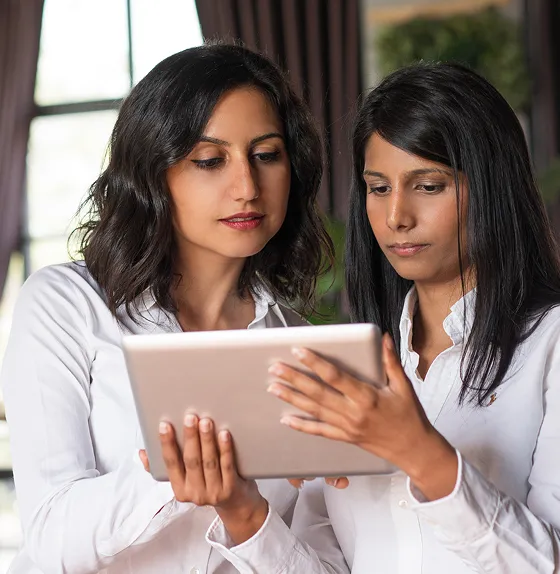Two women in white shirts looking at a tablet together in an indoor setting.