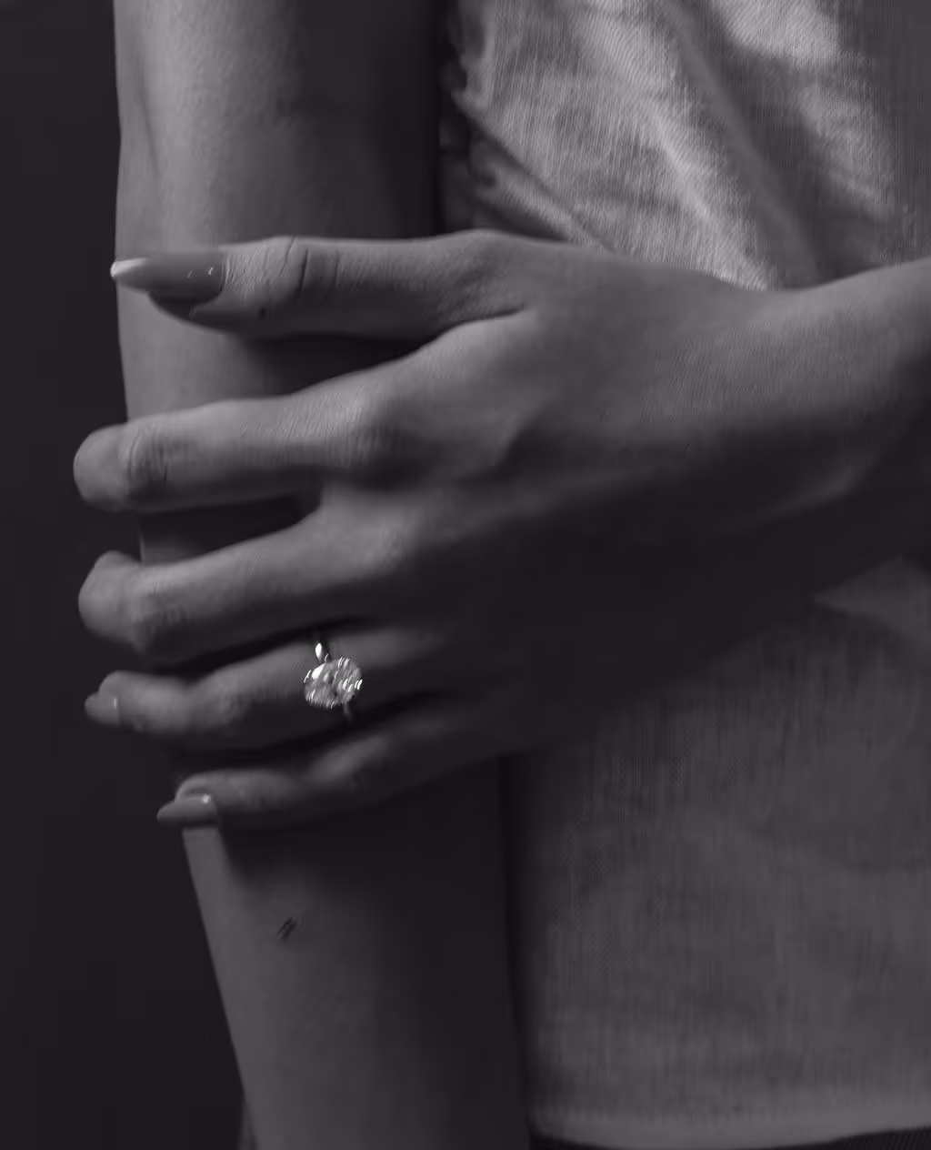 Close-up black-and-white photo of a hand with a diamond ring gently holding an arm.