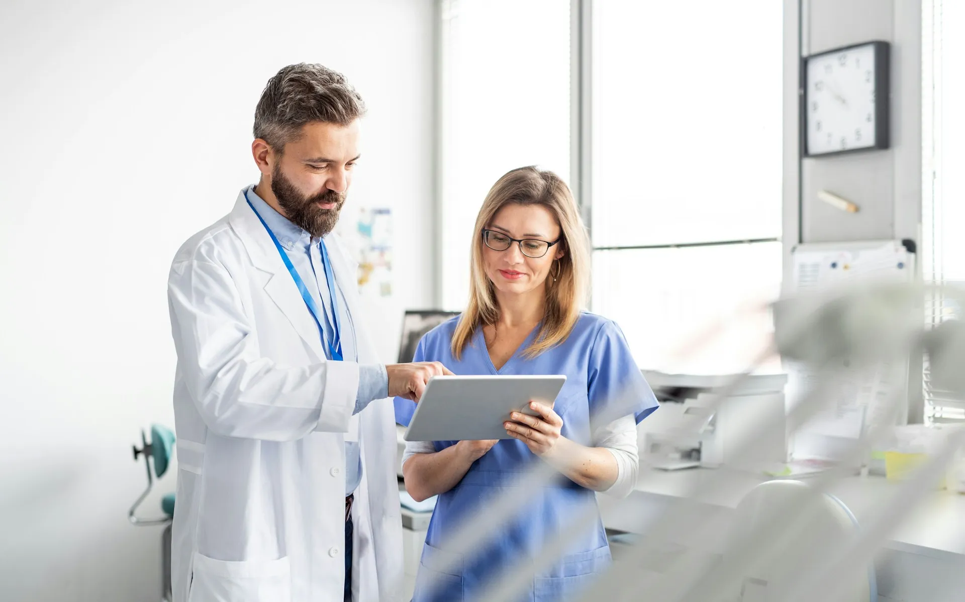 Male doctor and female nurse reviewing information on a digital tablet in a bright medical office.
