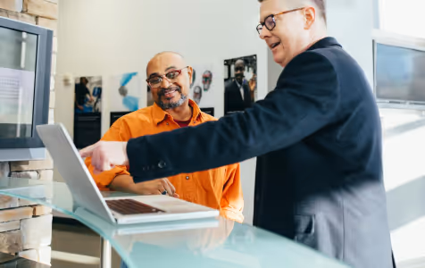 Young woman with long brown hair wearing a light cardigan over a black top sitting on a black leather chair in an office setting.