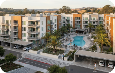 Modern apartment complex with a central swimming pool, surrounded by palm trees and lounge chairs, and covered parking spaces.