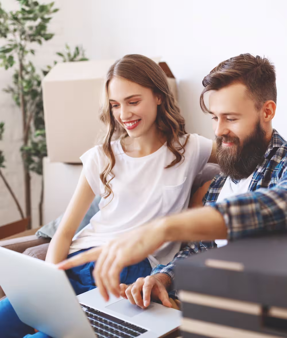 Smiling young couple sitting on a couch looking at a laptop together enjoying their fast home internet.