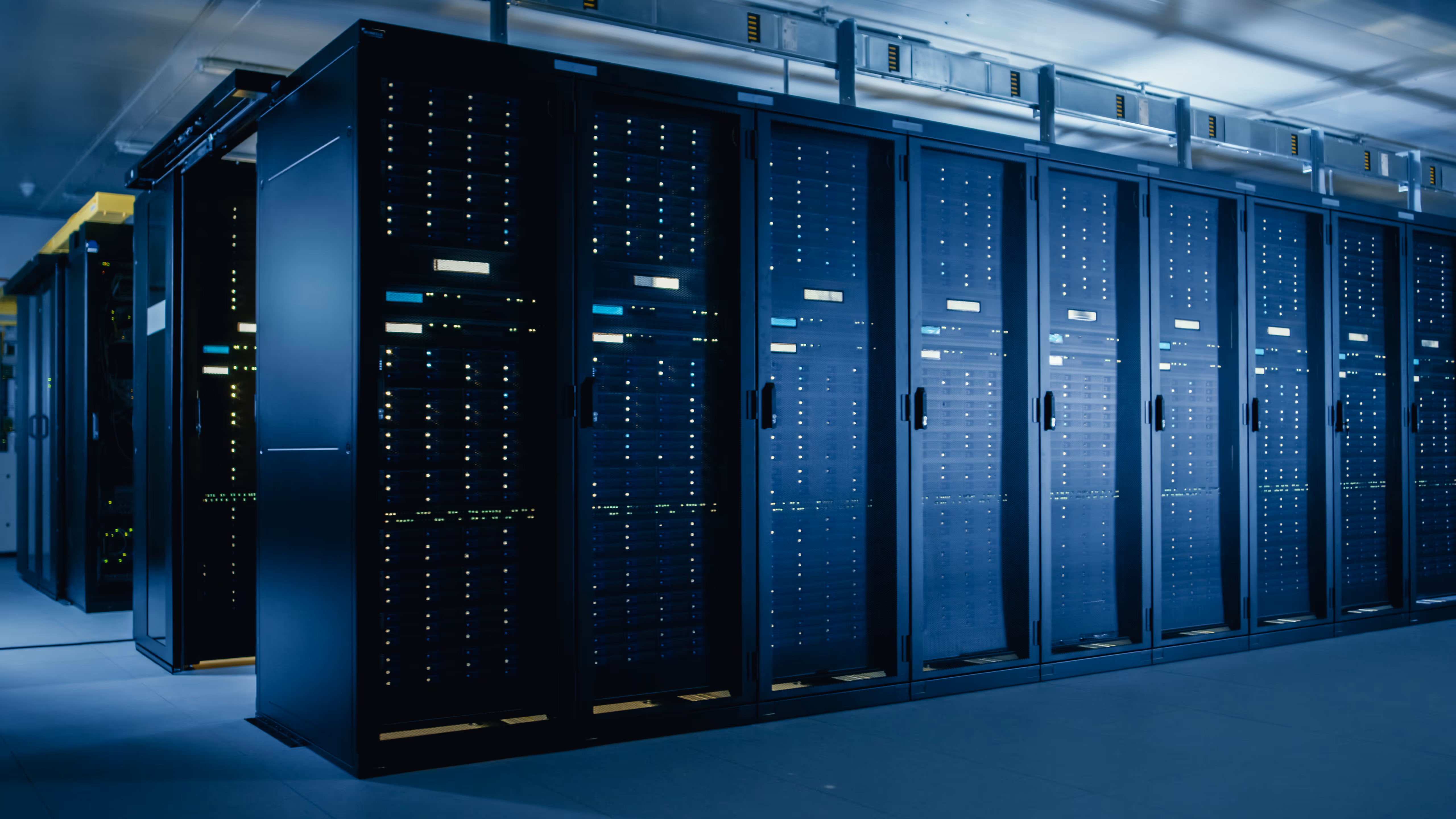 Modern data center room with rows of black server racks illuminated by blue ambient lighting.