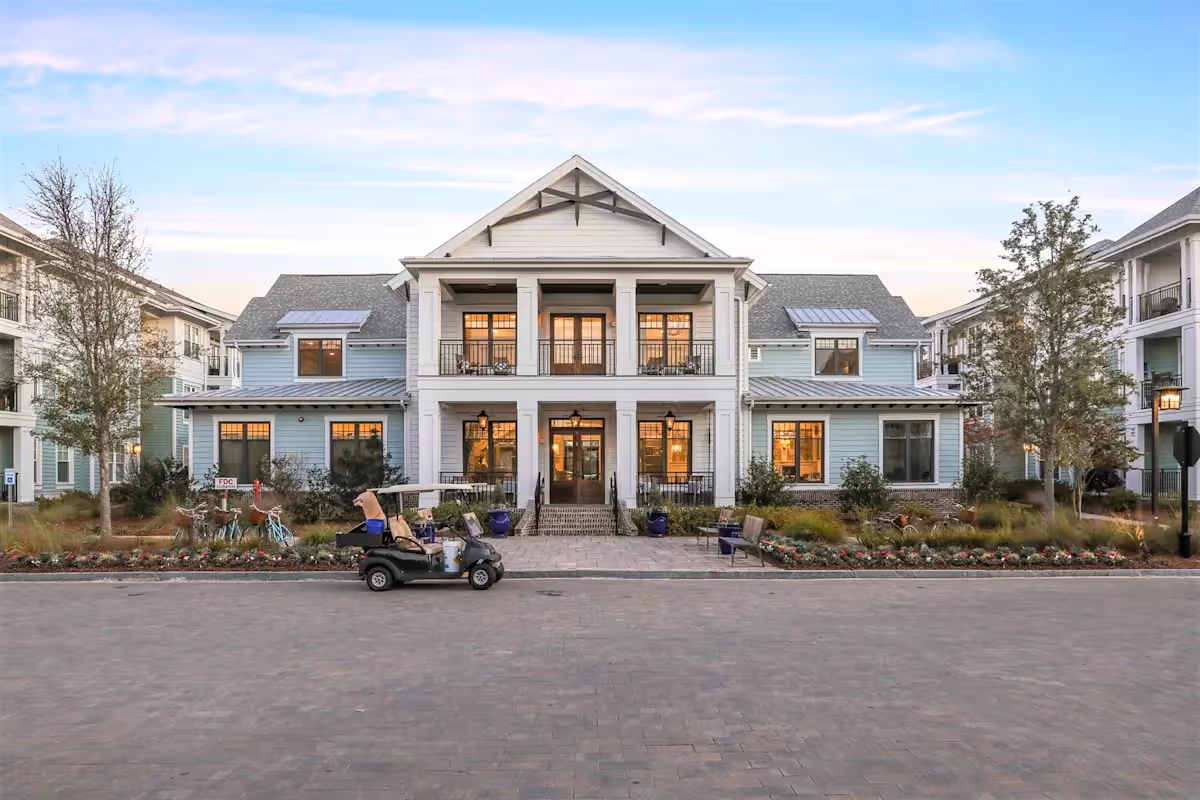 Large two-story residential building with blue siding, white columns, balconies, and a golf cart parked in front on a paved driveway.