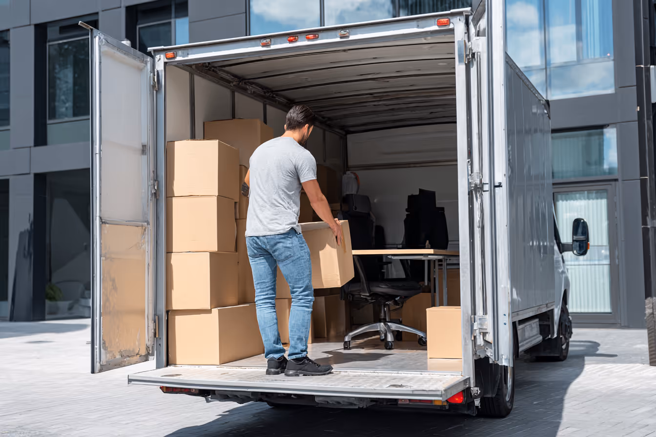 Person carrying a moving box inside a modern apartment, representing stressfreie Entrümpelung.