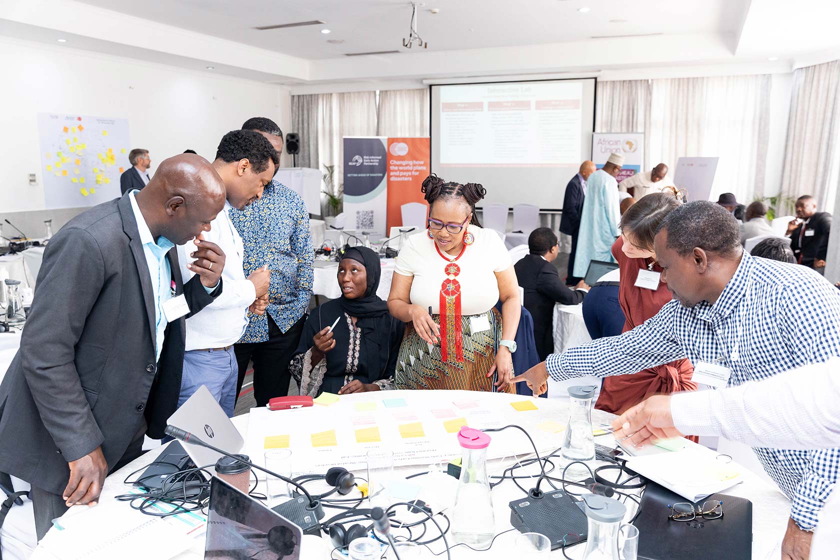Group of diverse professionals in a conference room engaged in discussion around a table with sticky notes and laptops.