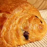 Close-up of a golden brown chocolate croissant on a wooden surface.