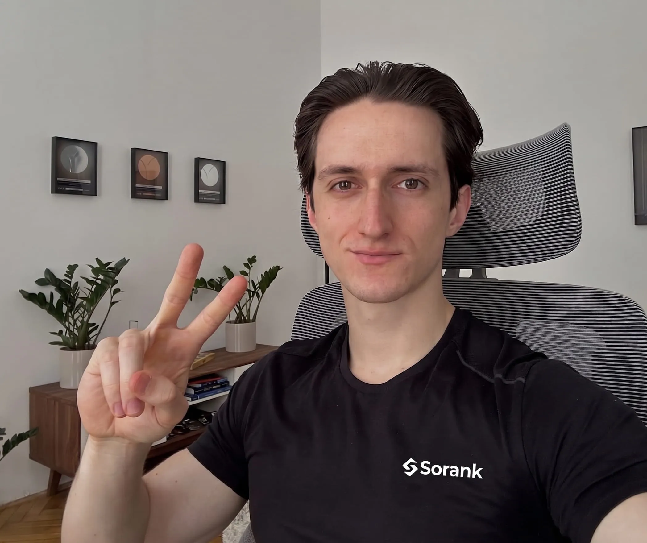 Man wearing a black Sorank shirt sitting on an office chair showing a peace sign with his hand.