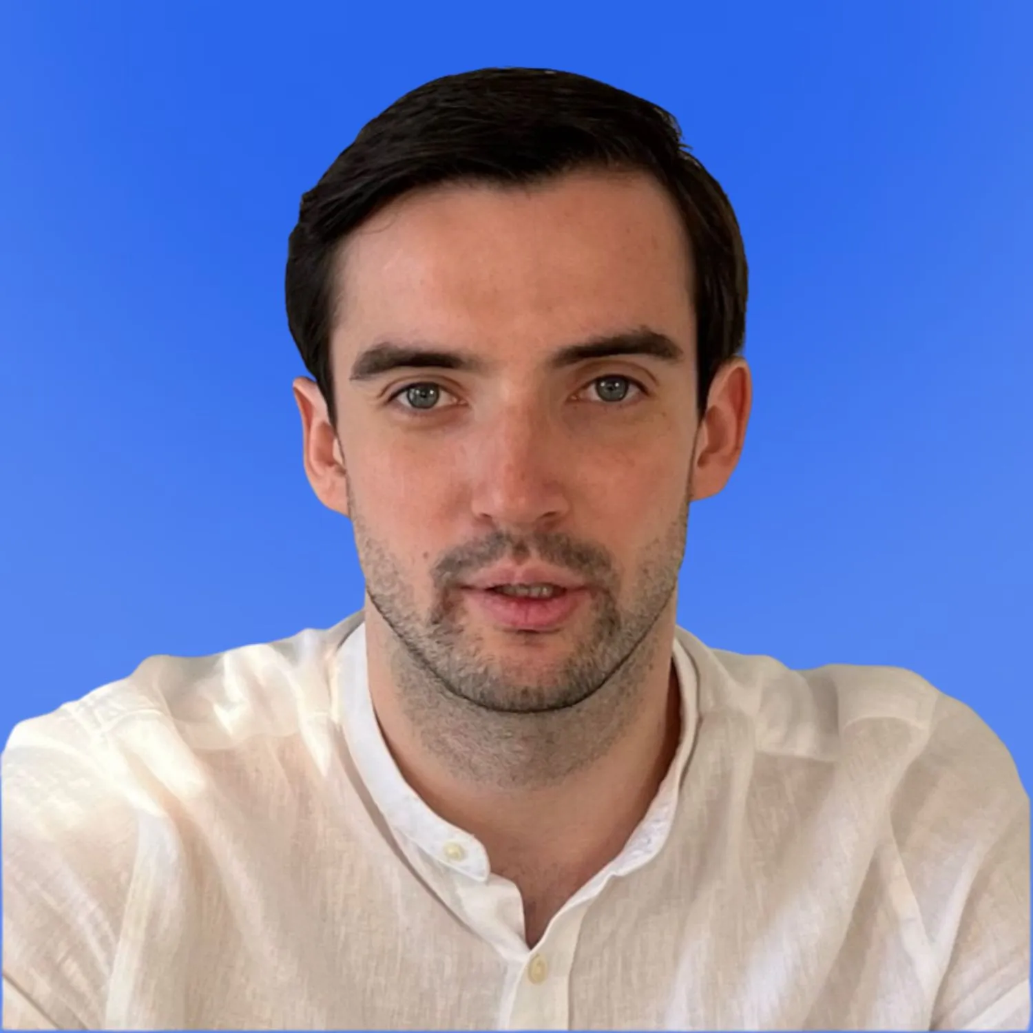 Portrait of a man with short dark hair and a light beard wearing a white linen shirt on a blue background