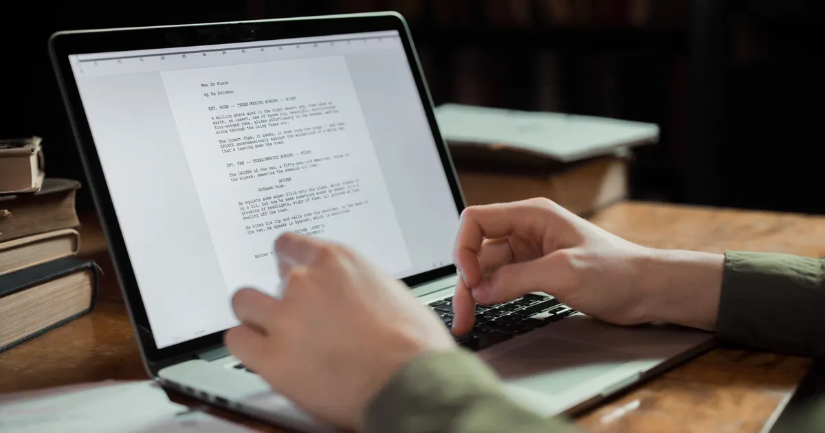 A writer typing an article on a laptop at a wooden desk