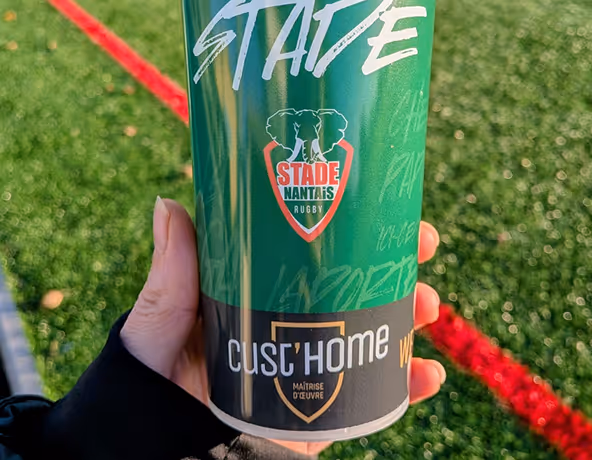 Gobelet aux couleurs du Stade Nantais avec logos partenaires, posé sur la pelouse.