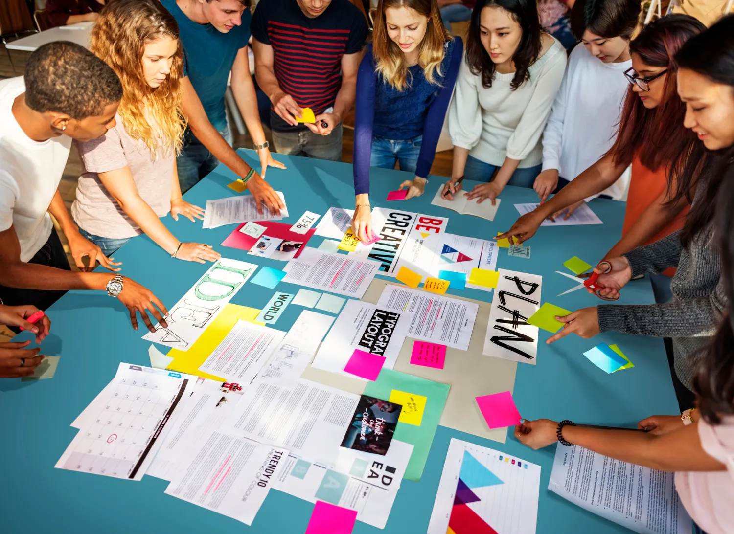 Group of diverse young adults collaborating over a table covered with documents, colorful sticky notes, and creative planning materials.