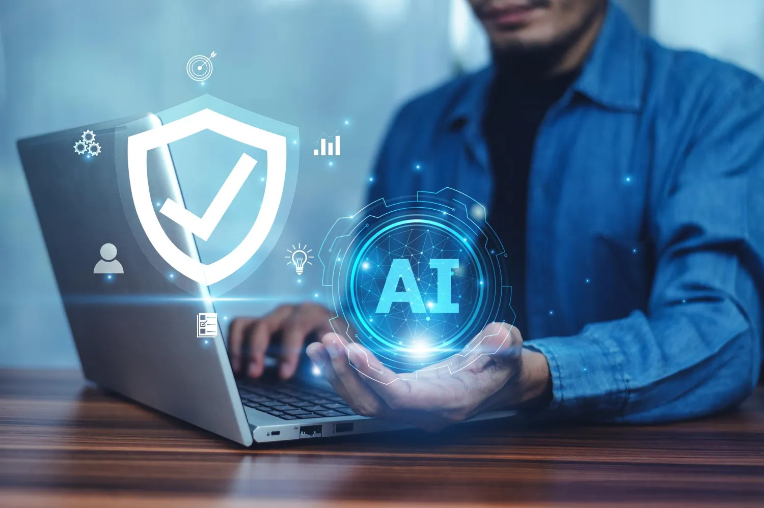 Person working on a laptop with digital icons of a shield checkmark and AI hologram floating above hands.