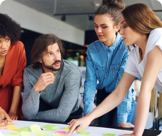 Four young professionals collaborating around a table covered with colorful sticky notes in a modern office.