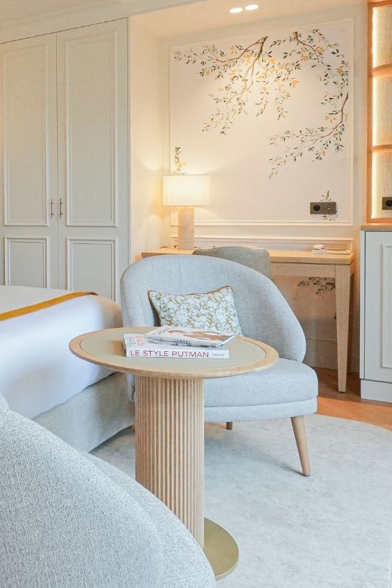 Coin salon d'une chambre avec deux fauteuils gris, table ronde avec livres, lampadaire et décoration florale murale.