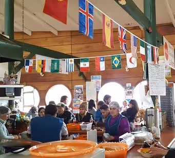Interior of a busy market cafe with people seated at tables and various international flags hanging from the ceiling.