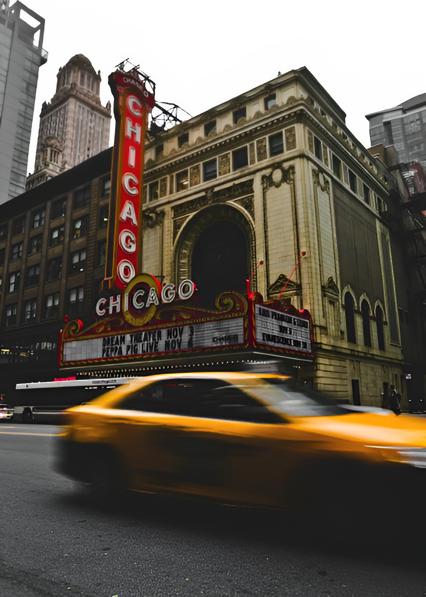 The iconic Chicago Theater with its illuminated vertical marquee at night, a yellow taxi speeding past in the foreground.