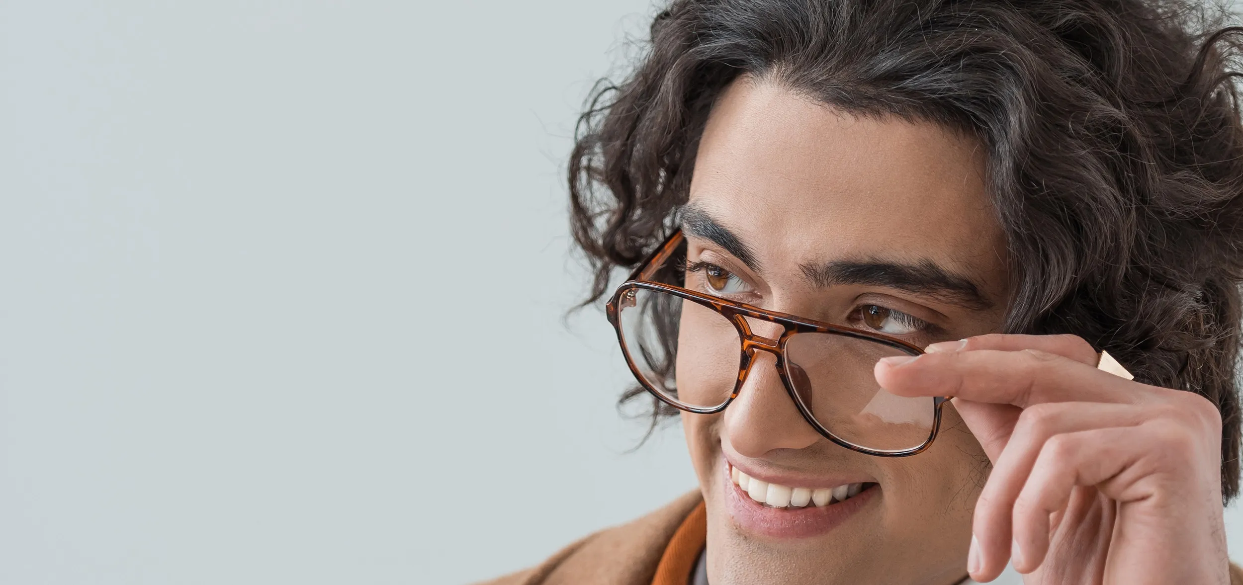 Person with curly hair smiling and adjusting tortoiseshell glasses