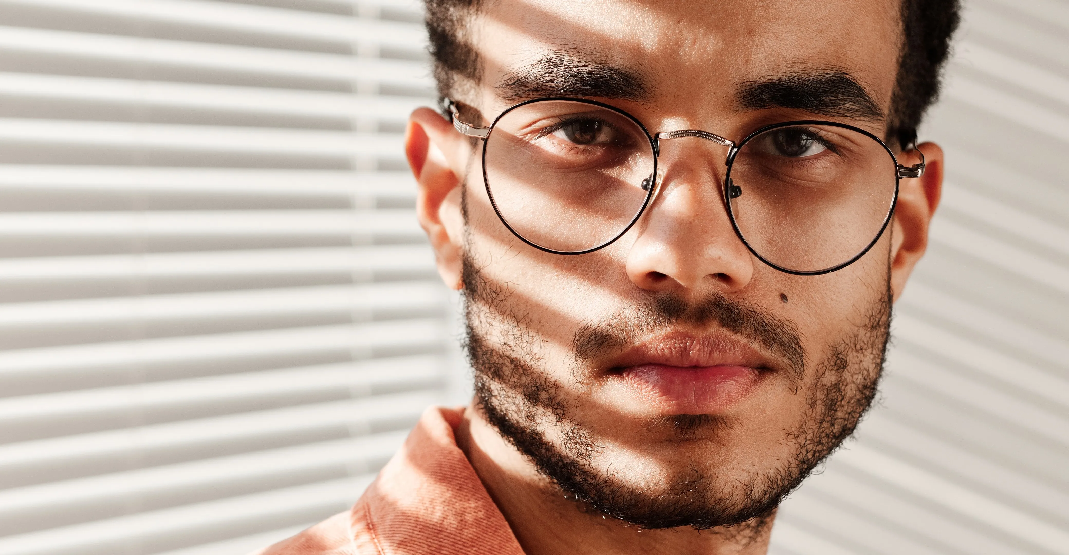 Person with round glasses and facial hair standing near striped background