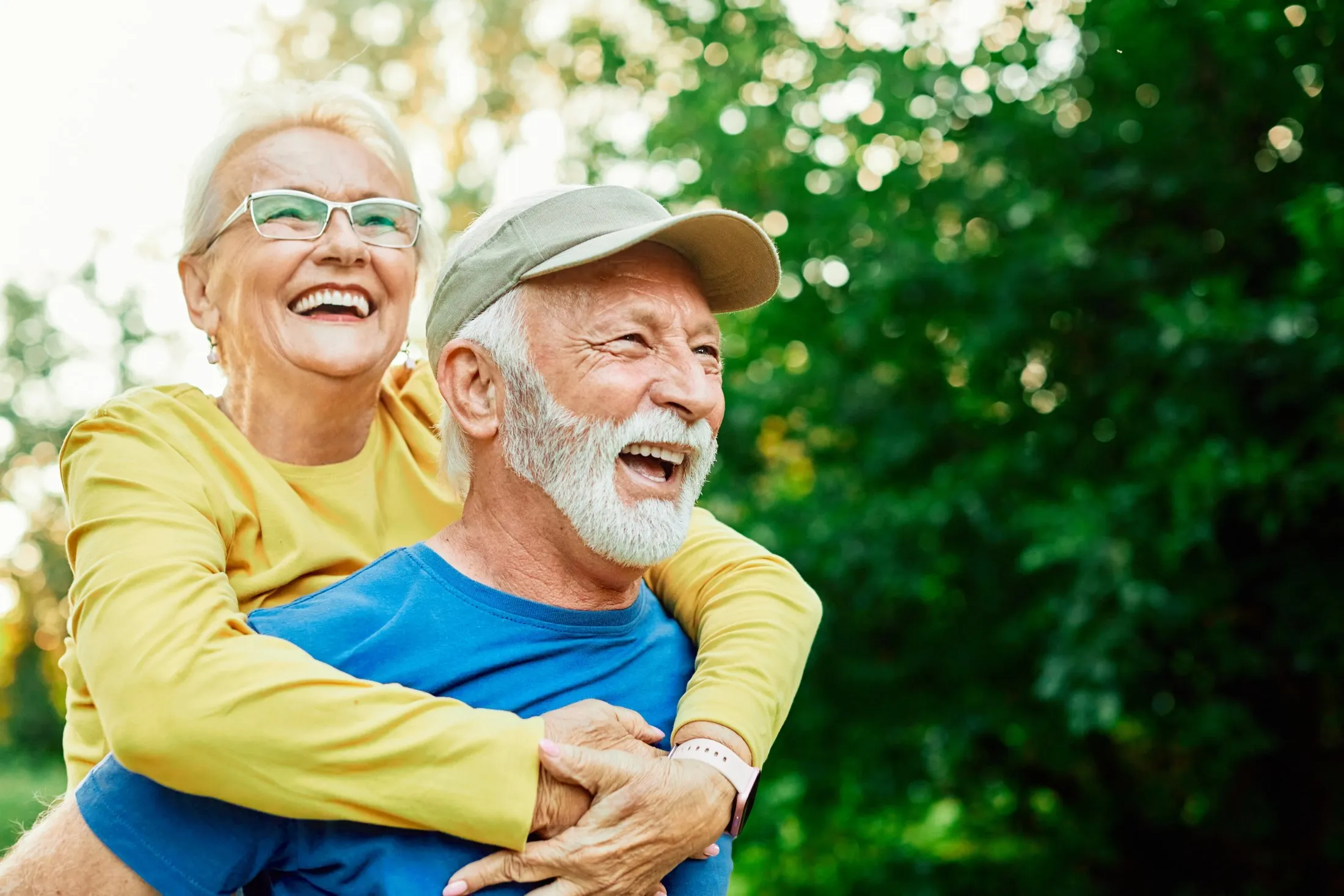 Elderly couple laughing and hugging outdoors on a sunny day