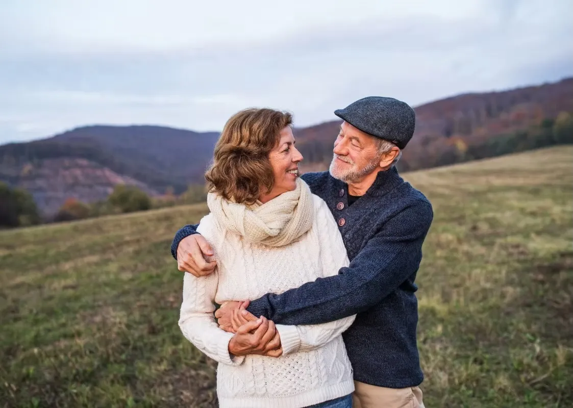 Elderly couple embracing and smiling in autumn mountain landscape