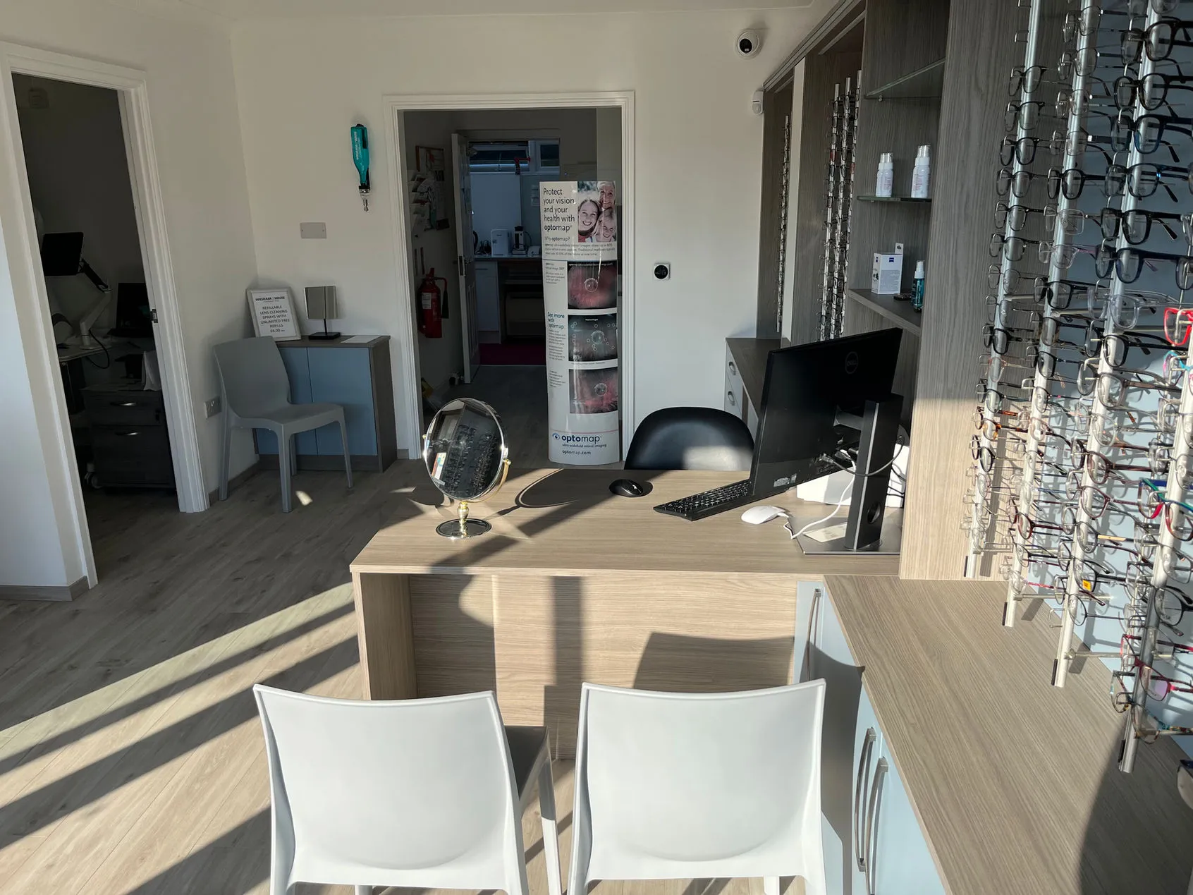 Optometrist office with desk, computer, eyeglass display, and Optomop poster