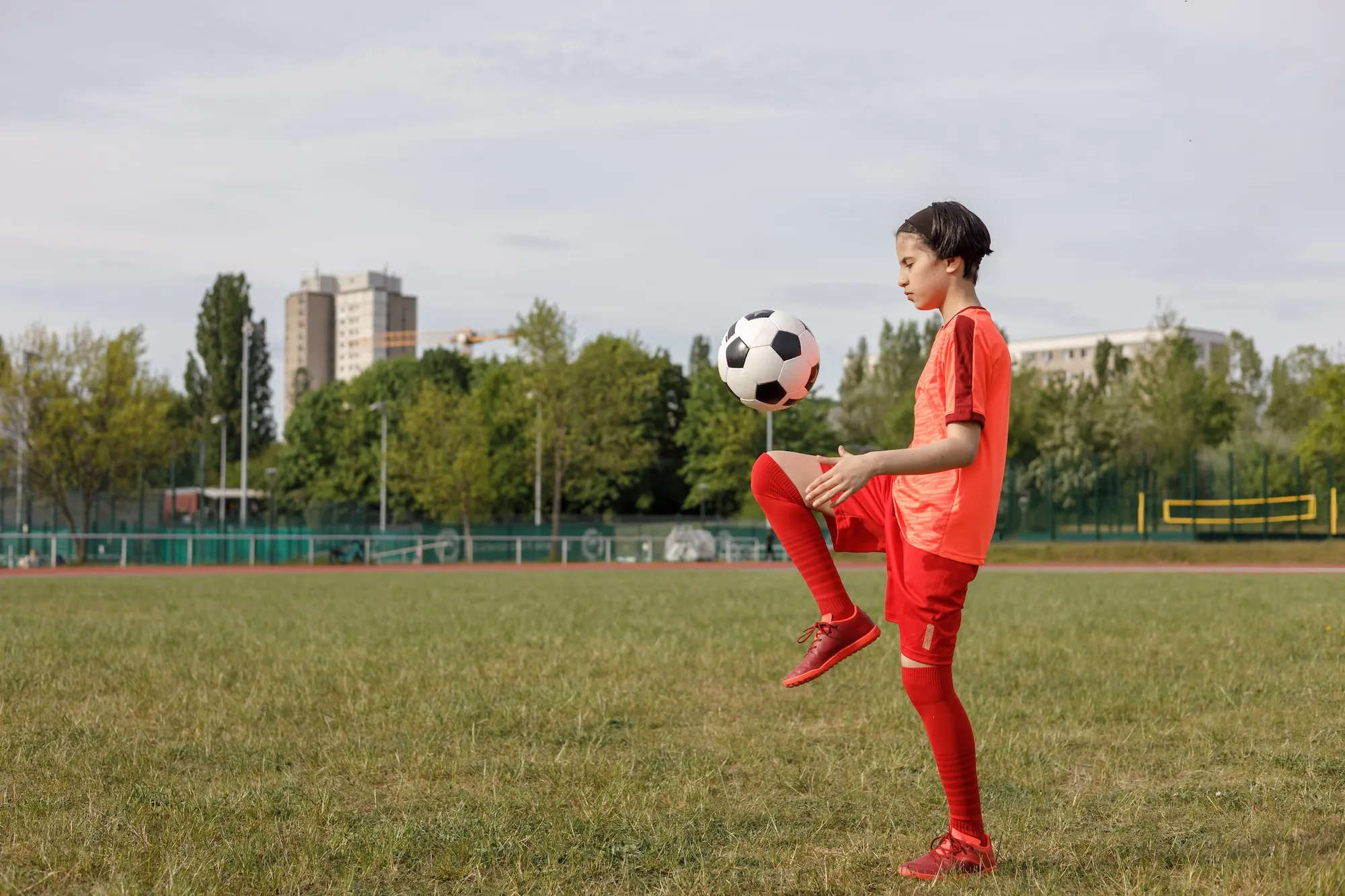 Young soccer player in red uniform balancing ball on knee outdoors