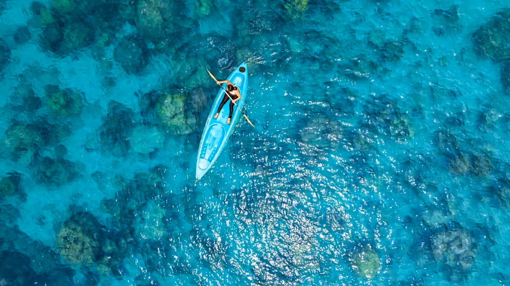 Woman on a pale blue kayak floating over azure blue water and a coral reef