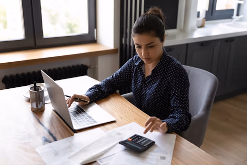 young woman works on her laptop and a calculator at a desk