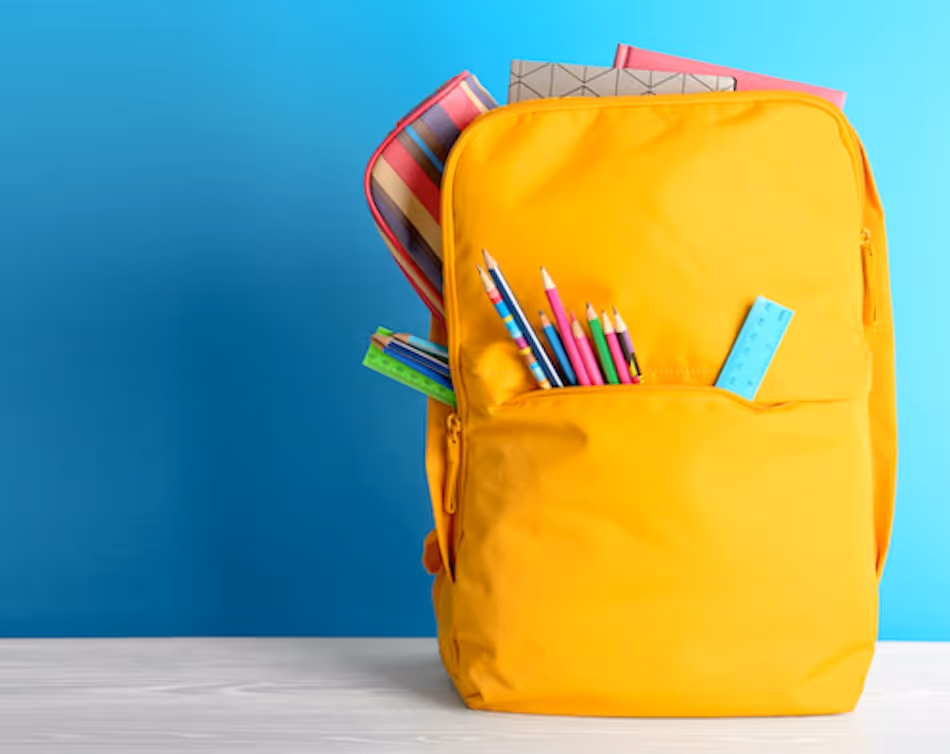 Yellow school rucksack stuffed with pens and a ruler on a white table