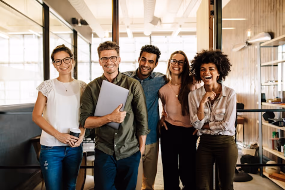 Group of five casually dressed people at work smiling at the camera
