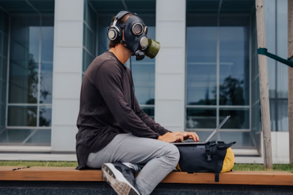 Man wearing a gas mask works on a laptop outside