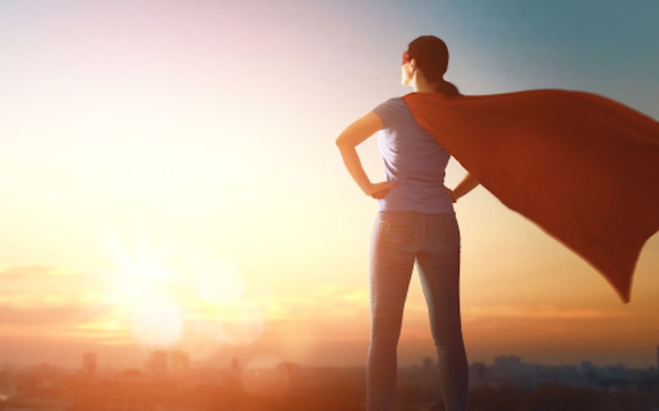 Woman with a super hero cape standing on a hill looking into the sunset