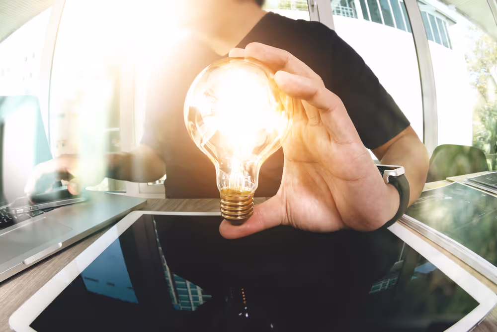 Person holding a lightbulb above a computer table