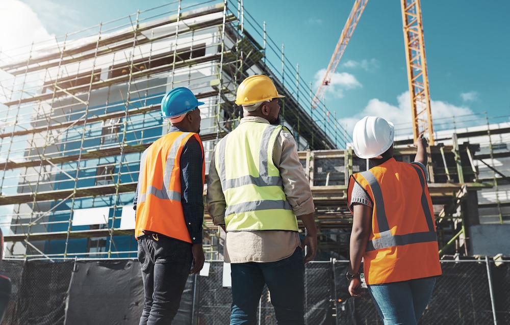 Group of three building consultants in hard hats survey a construction site 