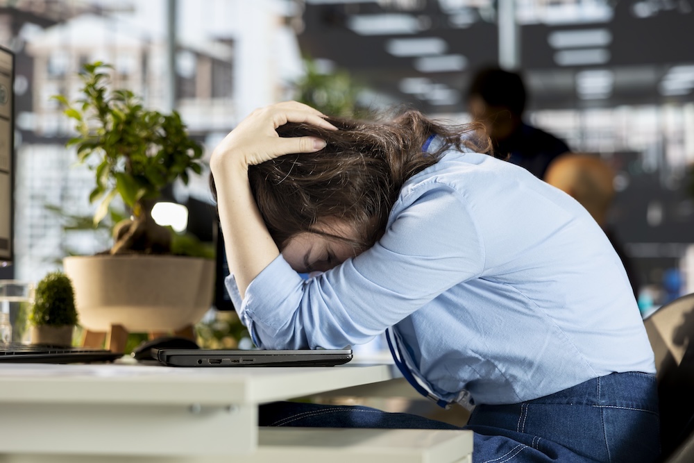 Young woman sits at her desk with her head in her hands over a closed laptop