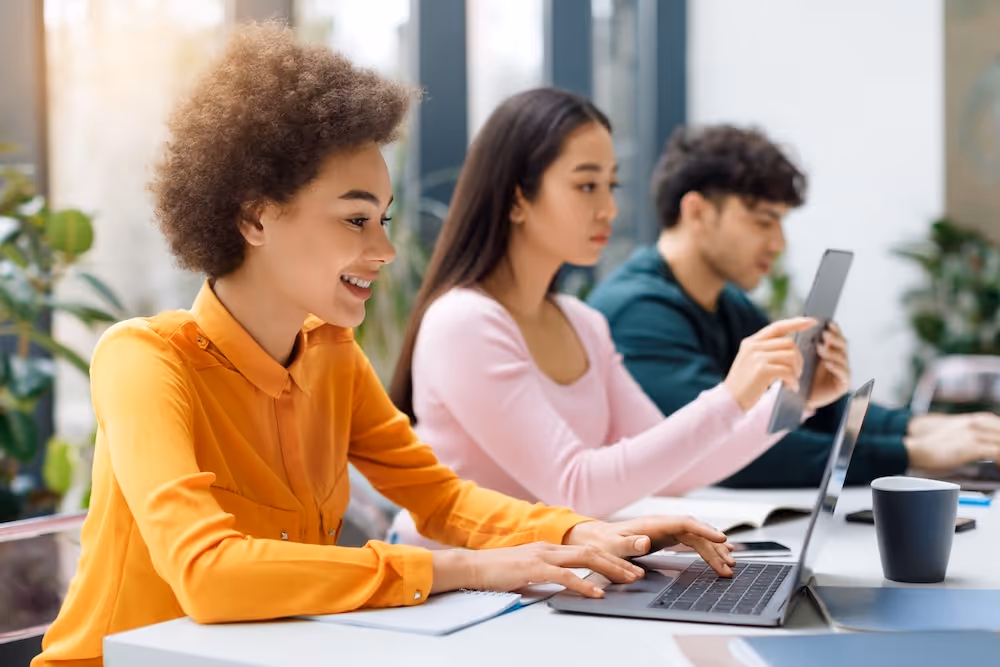 three employees work on laptops and tablets