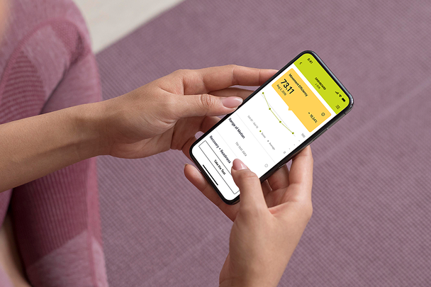 Person holding a smartphone displaying a health app with a yellow screen showing a heart rate average of 73.1 bpm and a graph.