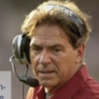 Coach wearing a headset with microphone and a red shirt, looking focused outdoors.