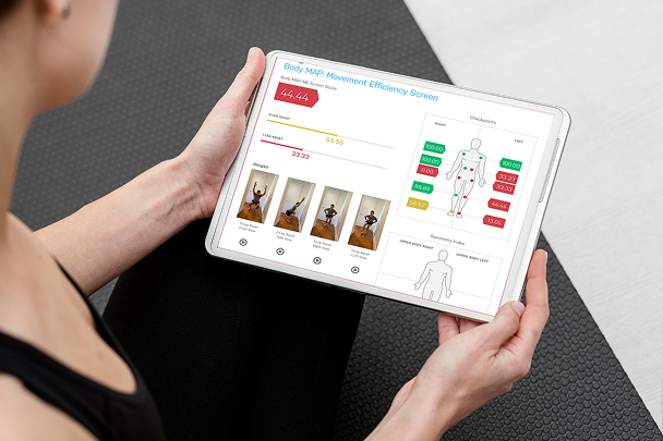Person holding a tablet displaying a Body MAP Movement Efficiency Screen with scores, checkpoints on a human body diagram, and exercise images.