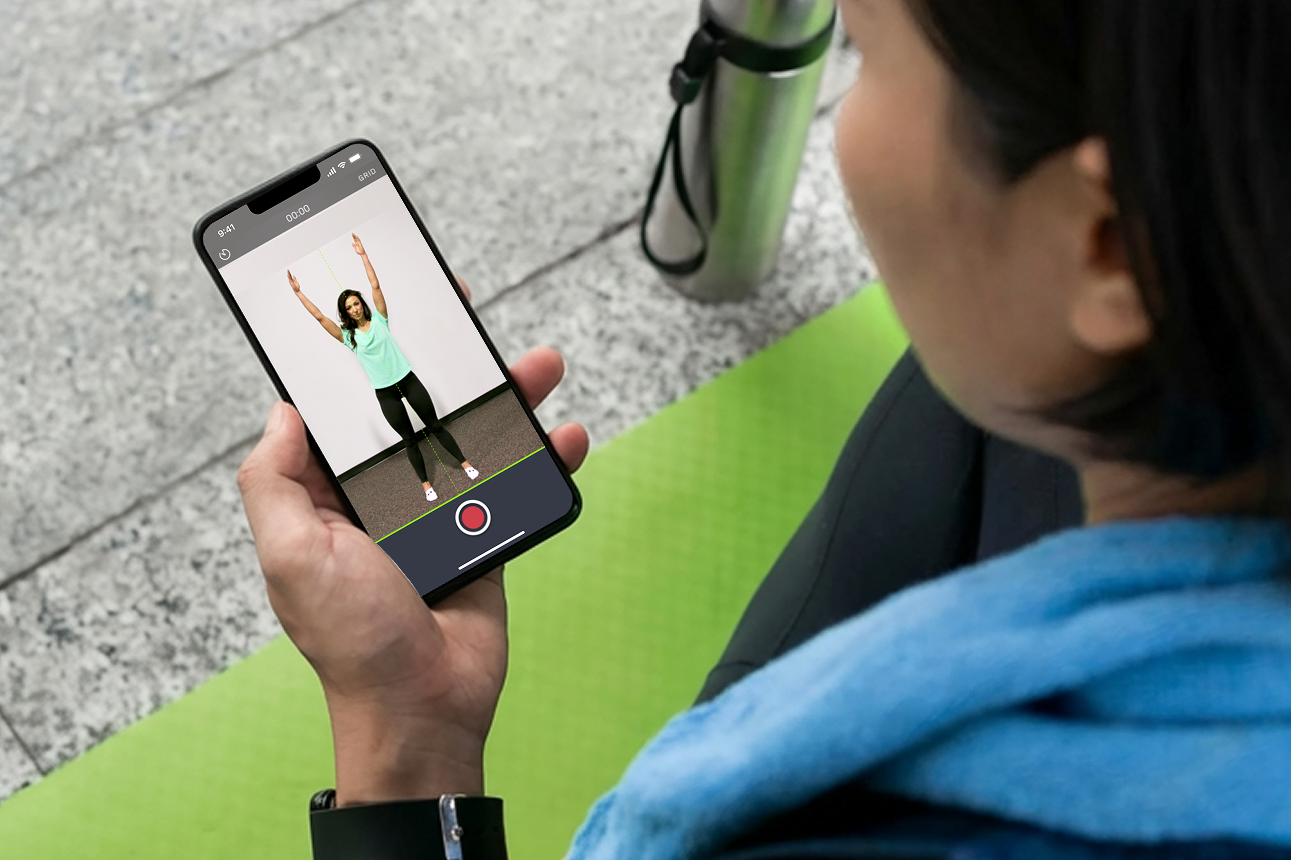 Person holding smartphone showing a video recording of a woman standing with arms raised indoors.