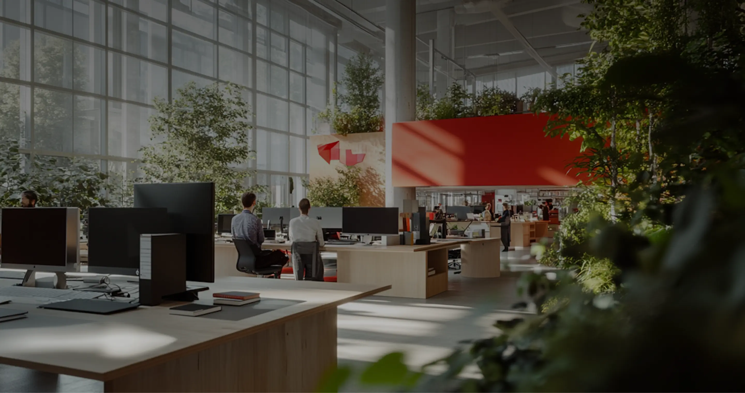 Modern open-plan office with large windows, multiple desks with computers, people working, and abundant greenery indoors.