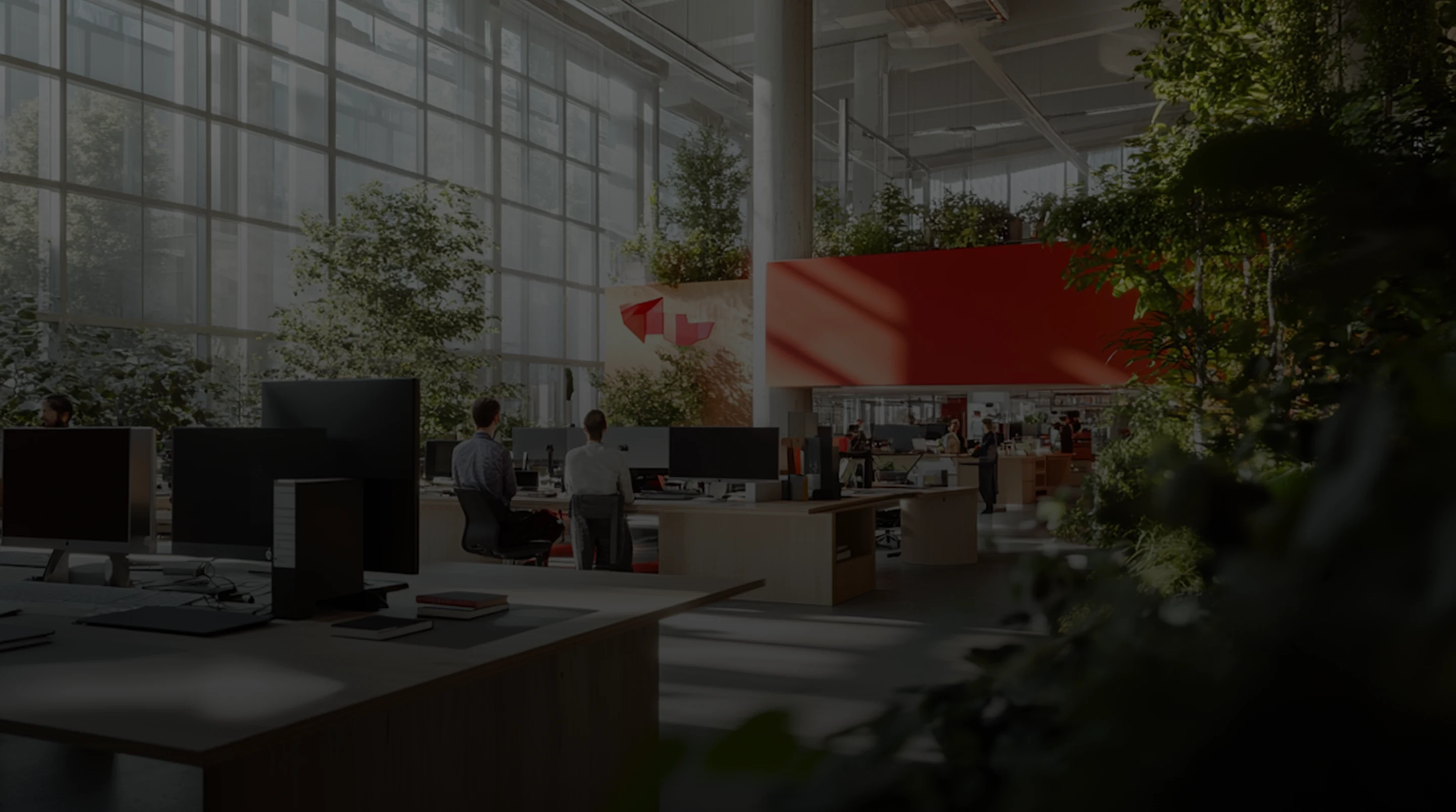 Modern open office space with large windows, plants, multiple desks with computers, and people working.