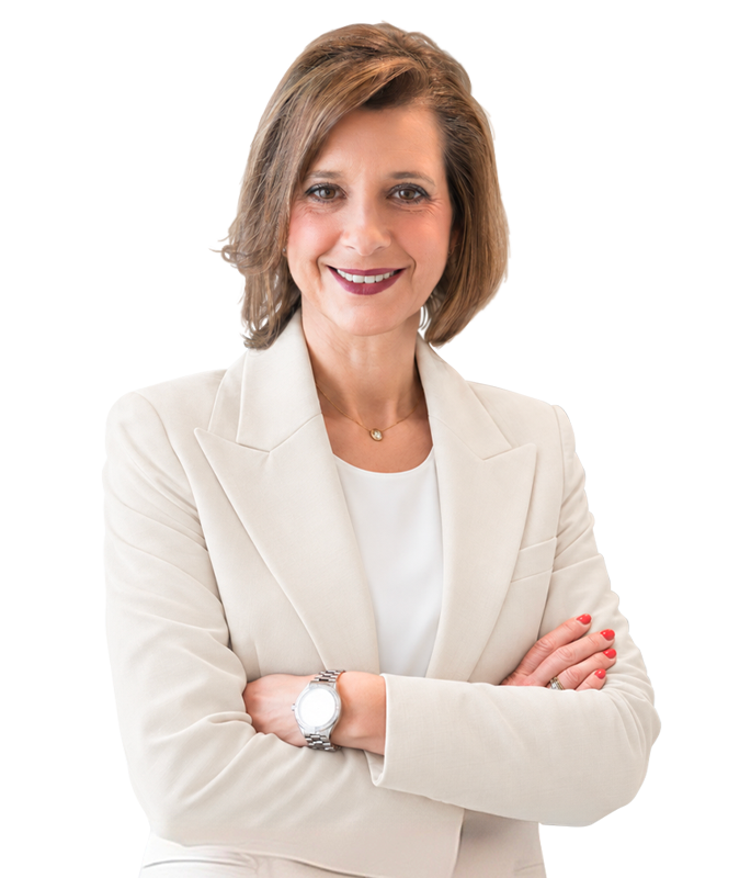 Confident woman with shoulder-length brown hair wearing a beige blazer and white blouse, arms crossed, smiling at the camera.